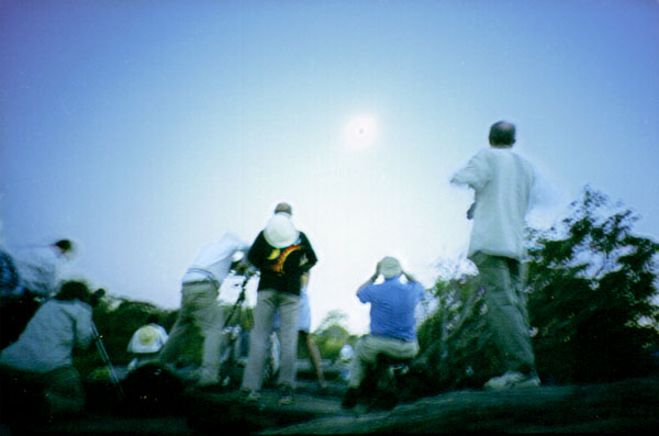 African Eclipse 2001!
When most people are taking closeups of the sun and its wonderful prominences, it is sometimes nice just to soak up the atmosphere. In the image above Greg has tried to show in a quick not-too-steady (hand-held) photograph the sheer intensity of everyone's interest in this first eclipse of the new millennium. Incidentally, this is the only picture Greg took during the eclipse. 
"The eclipse was one of the most spectacular astronomical events I have ever witnessed and what a wonderful country Zimbabwe is in which to have seen it!"
Link-words: Eclipse